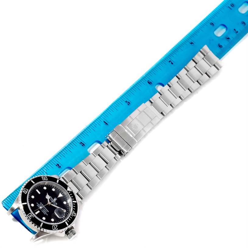 This image shows a top view of a Rolex Submariner 16610 Men
s Stainless Steel Black Dial 16610 Men
s Stainless Steel Black Dial watch, including the face, bezel, and bracelet, alongside a ruler.