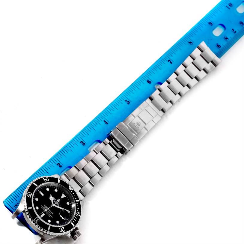 This image shows a Rolex Submariner 16610 Men
s Stainless Steel Black Dial 16610 Men
s Stainless Steel Black Dial watch lying flat with its face and metal bracelet visible next to a blue ruler.
