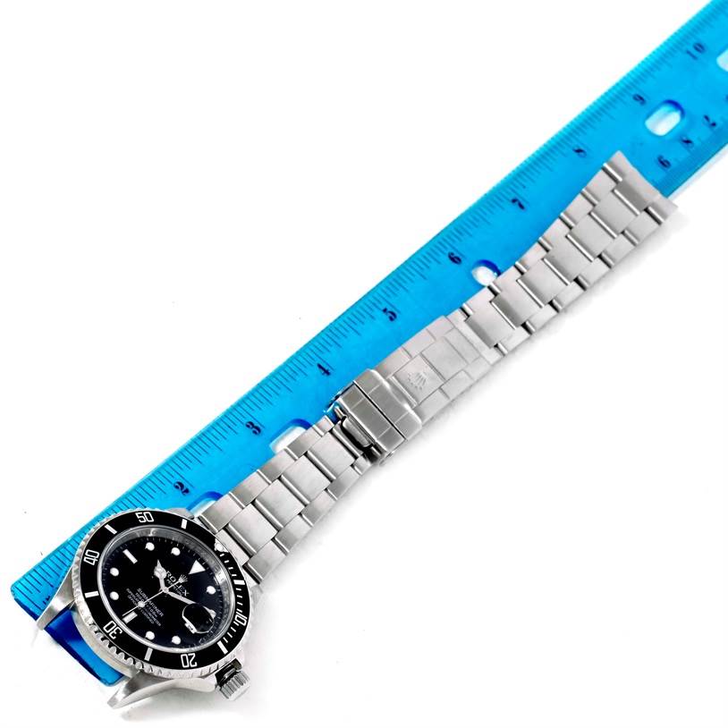 The image shows the Rolex Submariner 16610 Men
s Stainless Steel Black Dial 16610 Men
s Stainless Steel Black Dial watch laying flat with its bracelet extended alongside a ruler.