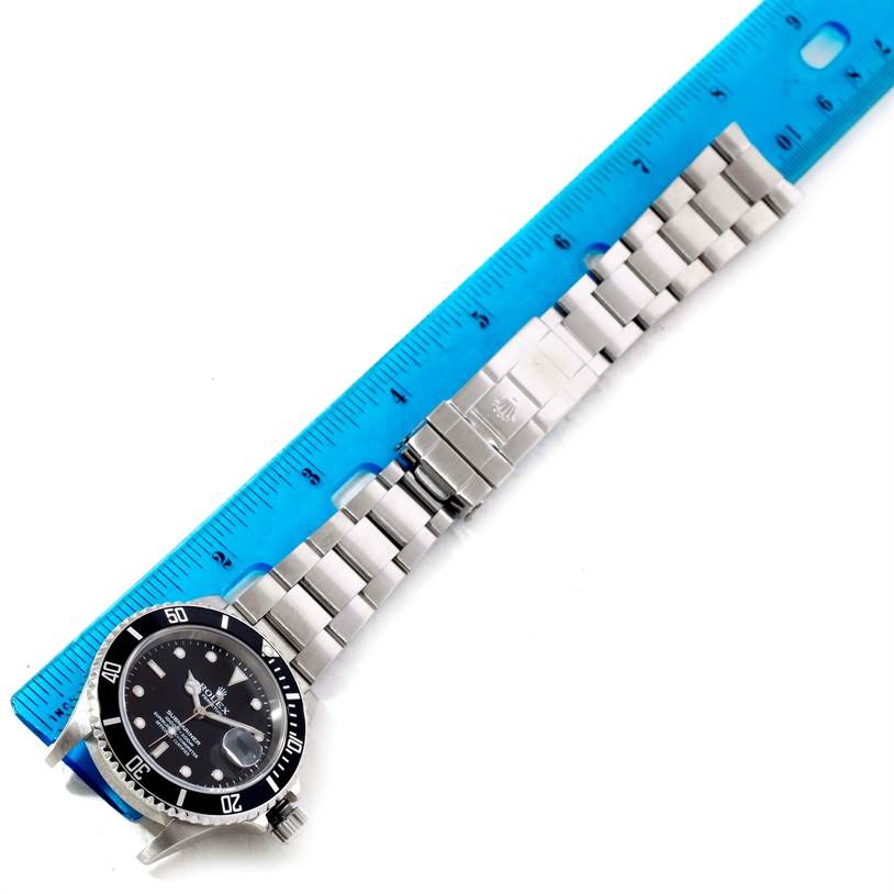 The Rolex Submariner 16610 Men
s Stainless Steel Black Dial 16610 Men
s Stainless Steel Black Dial watch is shown from a top view with a focus on its bracelet and dial alongside a blue ruler for scale.