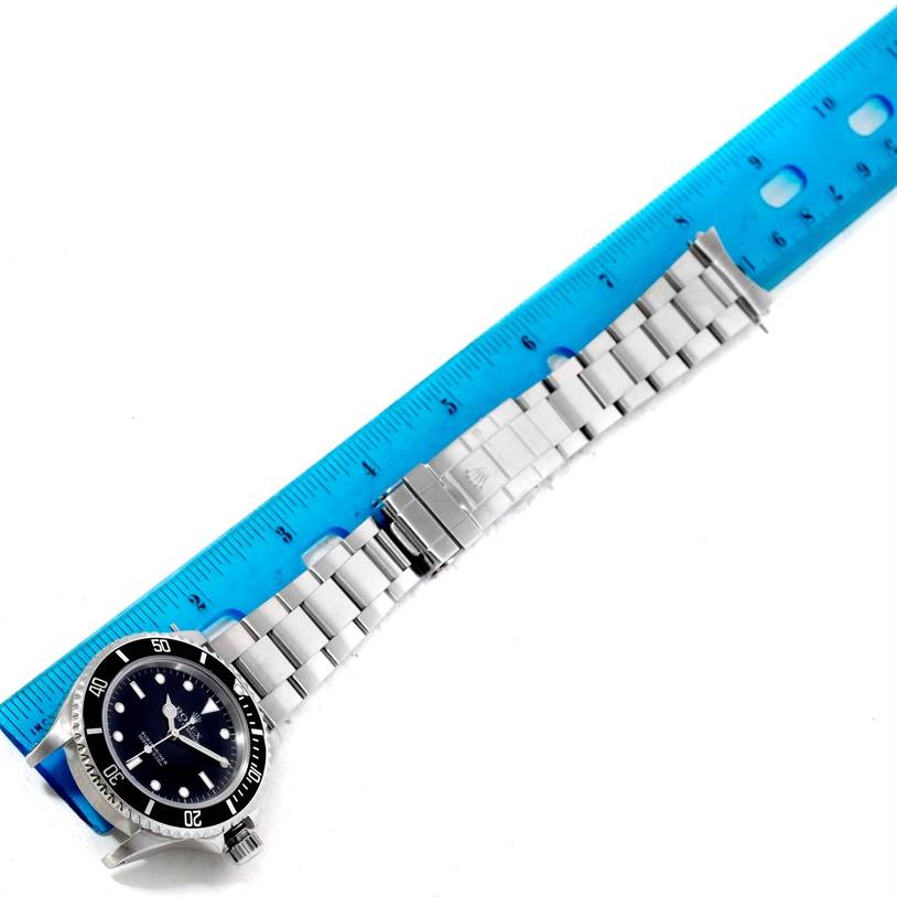 The image shows a Rolex Submariner 14060 Men
s Black Dial 14060 Men
s Black Dial watch laid flat with an extended metal bracelet next to a blue ruler for scale.