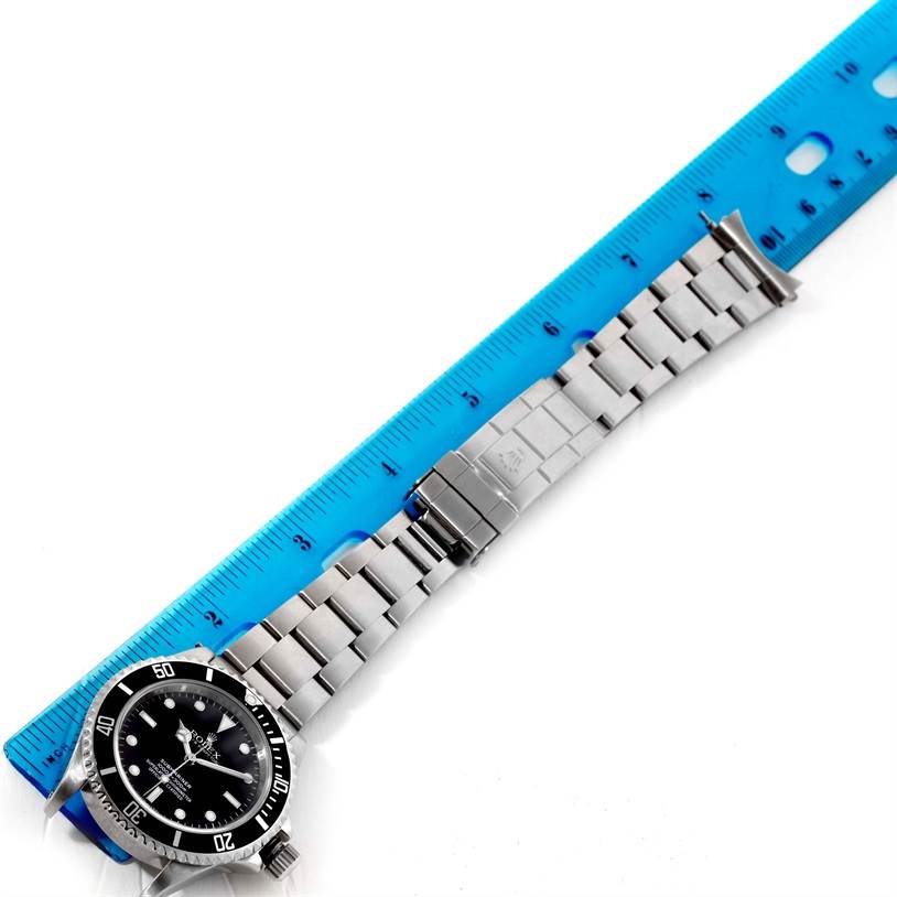 The Rolex Submariner 14060 Men
s Stainless Steel Black Dial 14060 Men
s Stainless Steel Black Dial watch is shown from a top-down angle, highlighting its face and metal bracelet alongside a blue ruler.