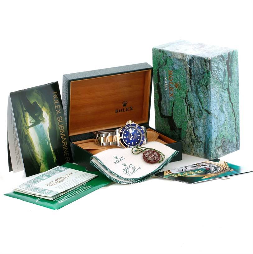 The image shows a Rolex Submariner 16613 Men
s Steel and Gold (two tone) Blue Dial 16613 Men
s Steel and Gold (two tone) Blue Dial watch from a front angle, along with its open box, manuals, and accessories.