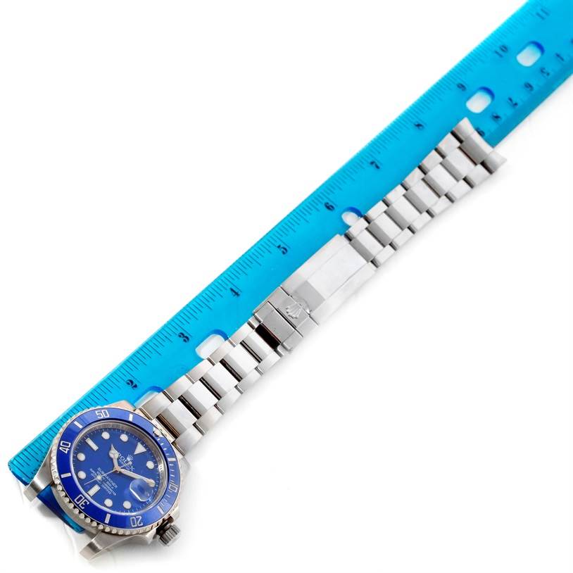 The image shows a horizontal view of a Rolex Submariner 116619LB Men's White Gold Blue Dial 116619LB Men's White Gold Blue Dial watch with its stainless steel bracelet alongside a blue ruler.
