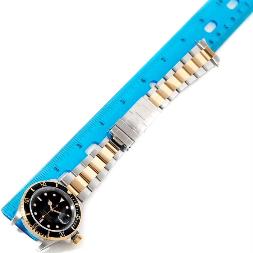 The watch is a Rolex Submariner 16613 Men
s Steel and Gold (two tone) Black Dial 16613 Men
s Steel and Gold (two tone) Black Dial shown from a top-down angle, fully extended with the band and a ruler for scale.
