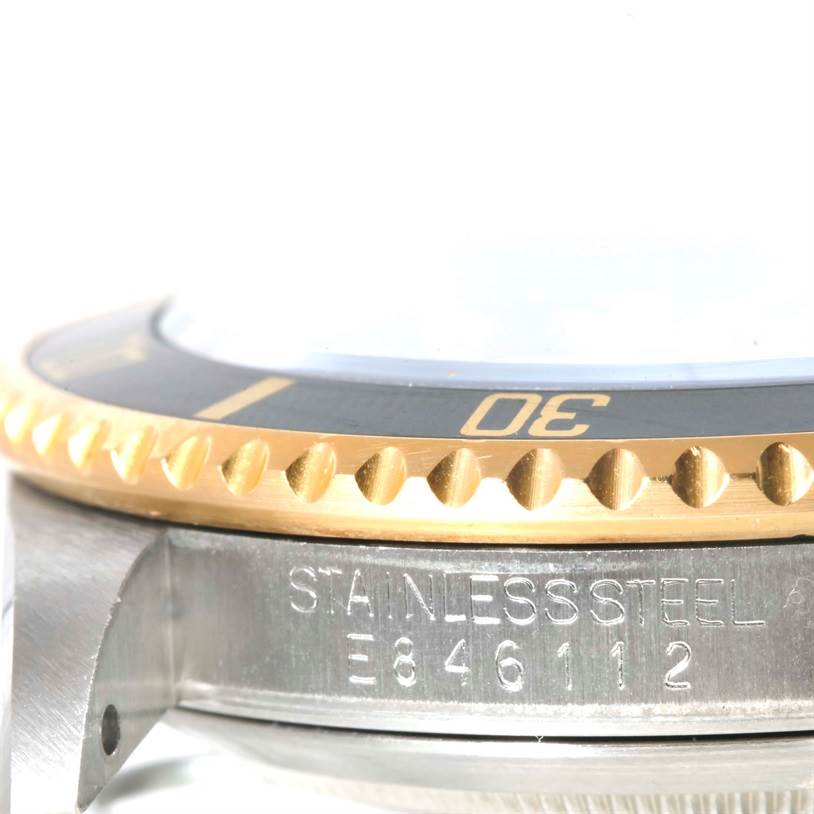 This close-up shows the side of the Rolex Submariner 16613 Men
s Steel and Gold (two tone) Black Dial 16613 Men
s Steel and Gold (two tone) Black Dial
s bezel and case, highlighting the stainless steel material and part of the serial number.