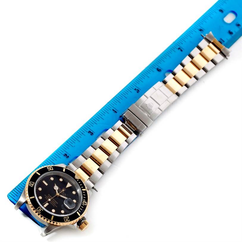 The image shows a Rolex Submariner 16613 Men's Steel and Gold (two tone) Black Dial 16613 Men's Steel and Gold (two tone) Black Dial watch laid flat, with emphasis on its dial, bezel, and bracelet, alongside a ruler for scale.