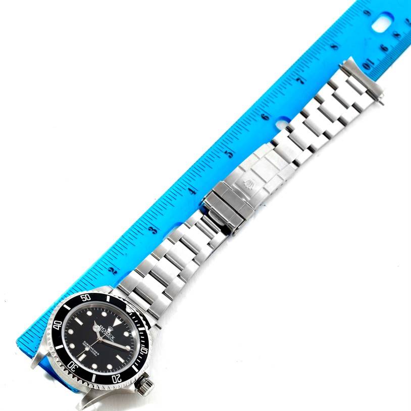 The image shows a top-down view of a Rolex Submariner 14060 Men
s Stainless Steel Black Dial 14060 Men
s Stainless Steel Black Dial watch with its stainless steel bracelet, alongside a blue ruler for scale.