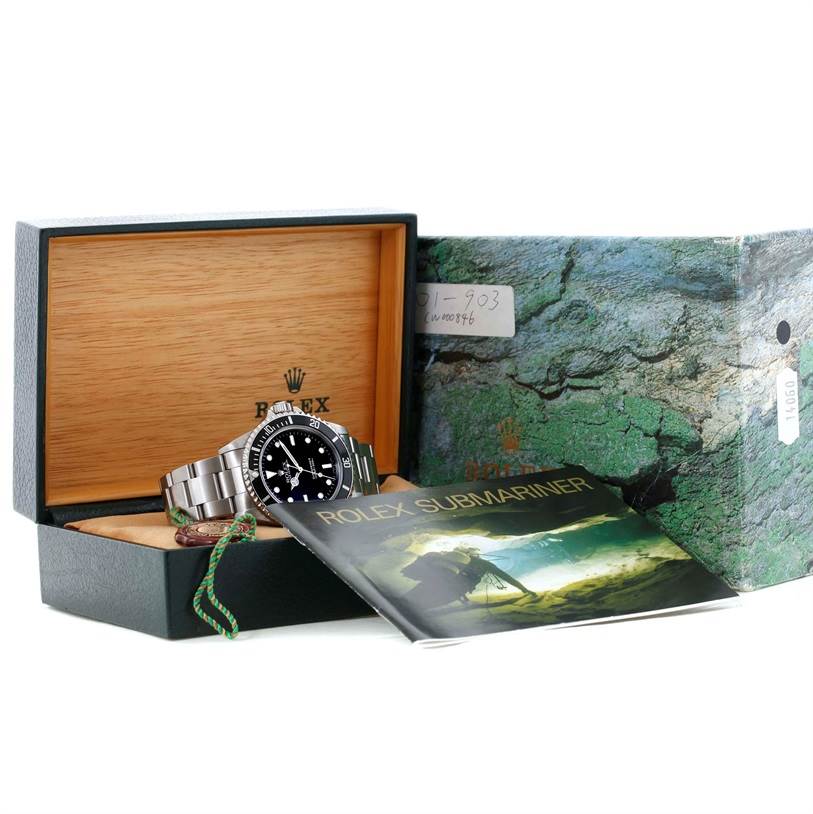The Rolex Submariner 14060 Men
s Stainless Steel Black Dial 14060 Men
s Stainless Steel Black Dial watch is pictured from an angled side view, inside its wooden box with a green outer box and a booklet.
