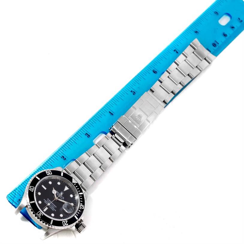 The Rolex Submariner 16610 Men
s Stainless Steel Black Dial 16610 Men
s Stainless Steel Black Dial watch is shown from a top view, displaying the face, bezel, and metal bracelet alongside a ruler.