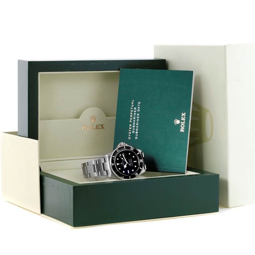 The image shows a Rolex Submariner 16610 Men
s Stainless Steel Black Dial 16610 Men
s Stainless Steel Black Dial watch resting on its opened green box with an instruction booklet beside it.