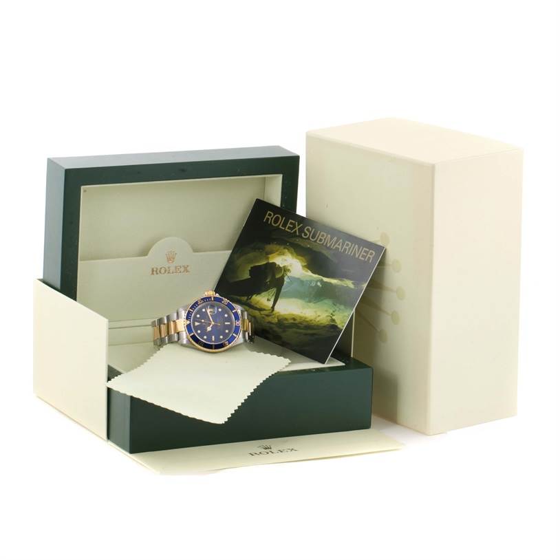 The image shows a Rolex Submariner 16613 Men's Steel and Gold (two tone) Blue Dial 16613 Men's Steel and Gold (two tone) Blue Dial watch in its box, along with a booklet and a cleaning cloth.