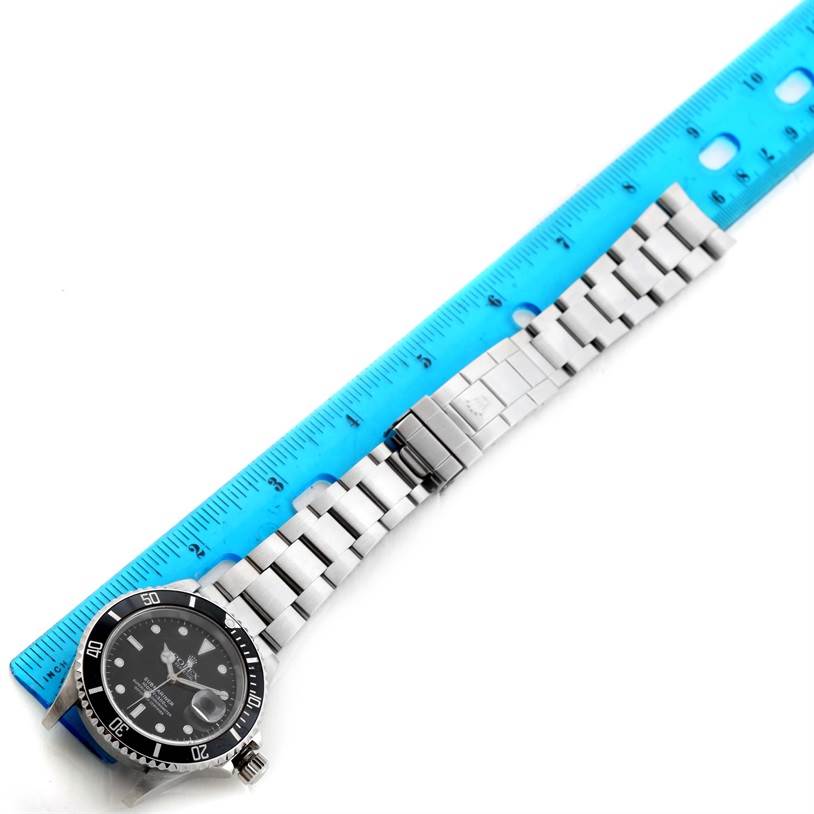 The image shows a top view of a Rolex Submariner 16610 Men
s Stainless Steel Black Dial 16610 Men
s Stainless Steel Black Dial watch with its bracelet aligned next to a blue ruler.