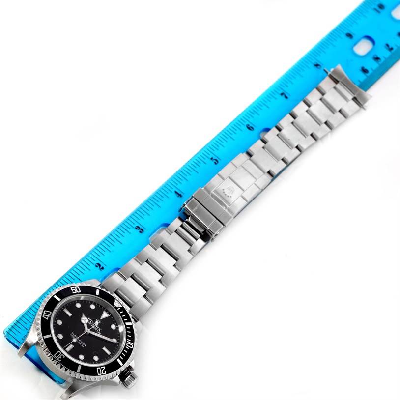 The image shows a Rolex Submariner 14060 Men
s Stainless Steel Black Dial 14060 Men
s Stainless Steel Black Dial watch, laid flat against a blue ruler, displaying the bracelet, clasp, and dial.