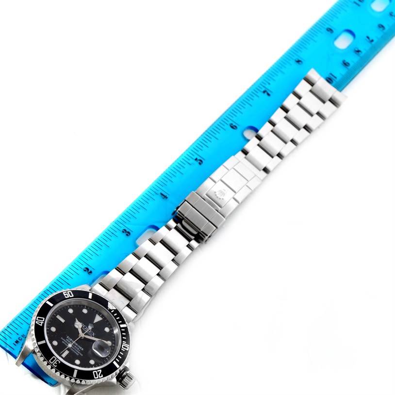 The Rolex Submariner 16610 Men's Stainless Steel Black Dial 16610 Men's Stainless Steel Black Dial watch is shown laid flat with its dial, bezel, bracelet, and clasp visible, next to a blue ruler.