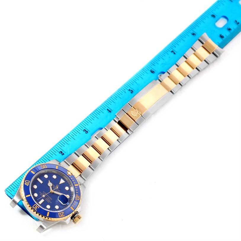 The image shows a top-down view of a Rolex Submariner 116613 Men's Steel and Gold (two tone) Blue Dial 116613 Men's Steel and Gold (two tone) Blue Dial watch beside a blue ruler, highlighting the face and band.