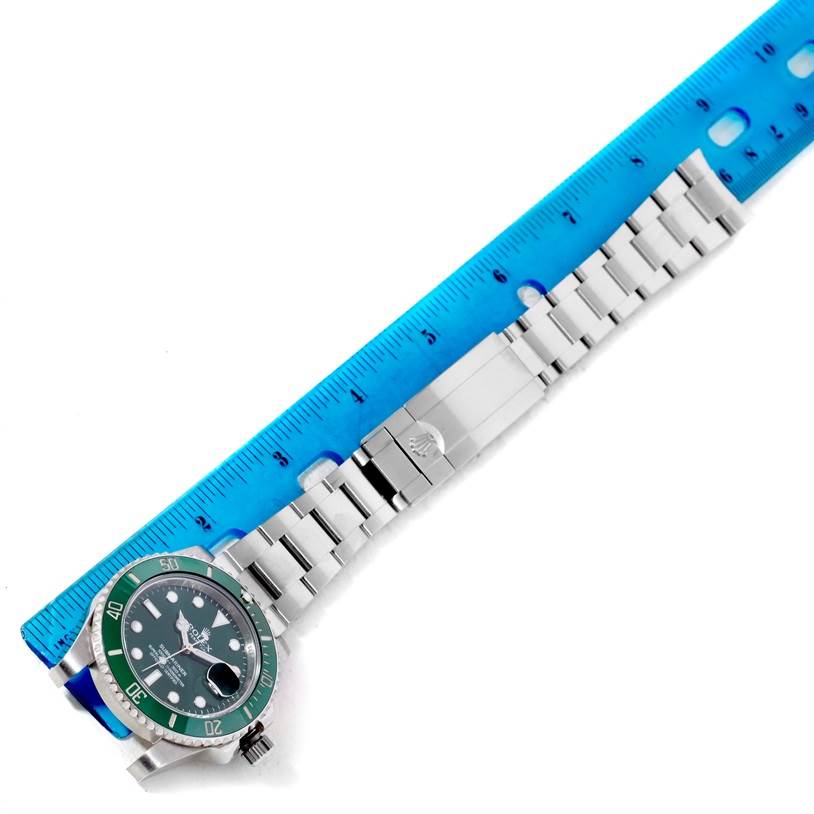 The Rolex Submariner 116610LV Men's Stainless Steel Green Dial 116610LV Men's Stainless Steel Green Dial watch is shown from an overhead angle, displaying the face, bezel, and bracelet next to a blue ruler.