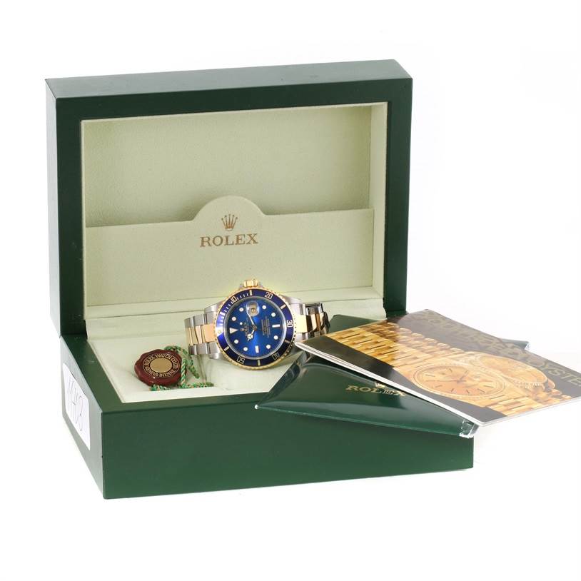 The photo shows a Rolex Submariner 16613 Men's Steel and Gold (two tone) Blue Dial 16613 Men's Steel and Gold (two tone) Blue Dial watch in its box, with a certificate and booklet beside it.