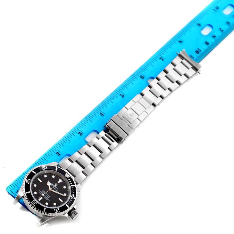 The Rolex Submariner 14060 Men
s Stainless Steel Black Dial 14060 Men
s Stainless Steel Black Dial watch is shown lying flat with its metal bracelet and clasp fully extended next to a ruler for measurement.