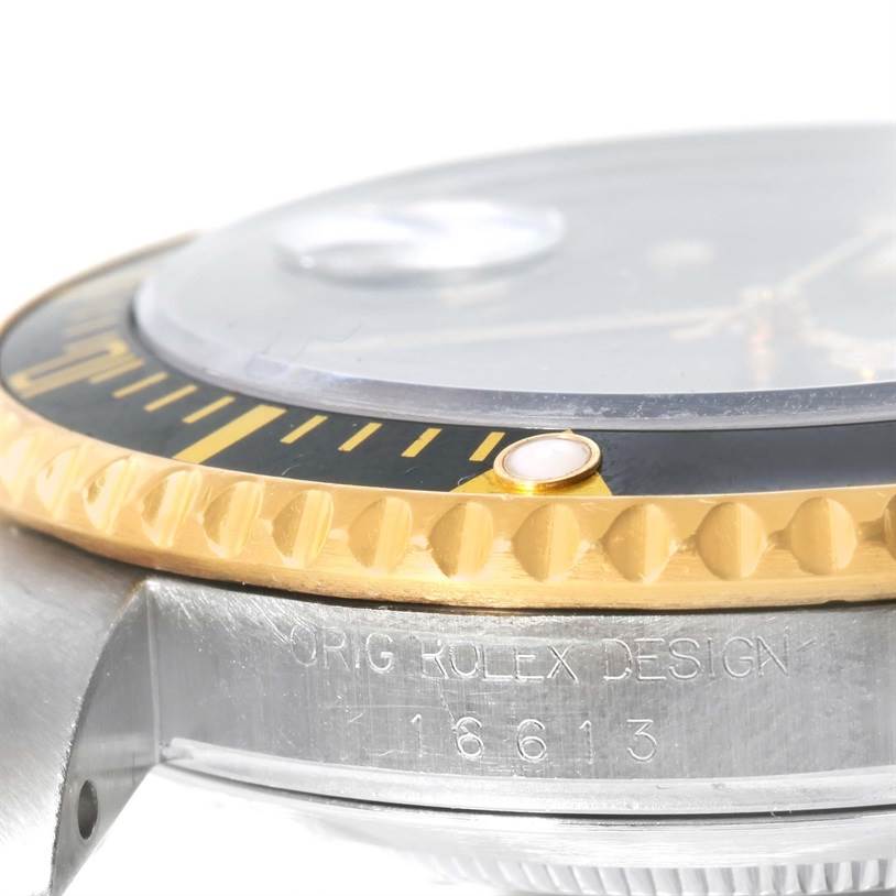 The image shows a close-up side view of the bezel, crystal, and engravings on the case of a Rolex Submariner 16613 Men's Steel and Gold (two tone) Black Dial 16613 Men's Steel and Gold (two tone) Black Dial watch.