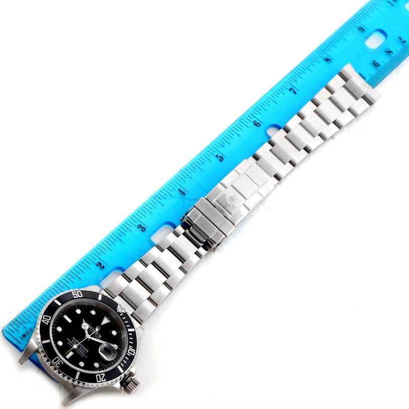 The Rolex Submariner 16610 Men
s Stainless Steel Black Dial 16610 Men
s Stainless Steel Black Dial watch is shown from a top-down angle, displaying the face, bezel, and bracelet with a measuring ruler beside it.