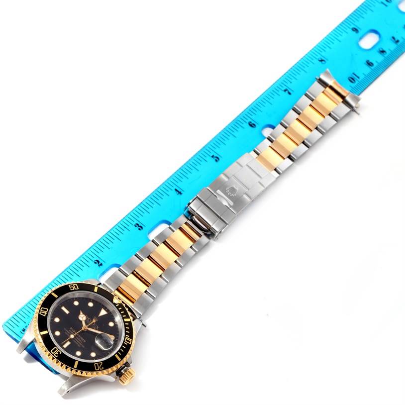 The image shows a top view of a Rolex Submariner 16613 Men's Steel and Gold (two tone) Black Dial 16613 Men's Steel and Gold (two tone) Black Dial watch, including the dial, bezel, and bracelet next to a ruler.