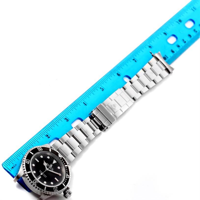 The image shows a Rolex Submariner 14060 Men
s Stainless Steel Black Dial 14060 Men
s Stainless Steel Black Dial watch laid flat with its face, bezel, bracelet, and clasp visible, along with a blue ruler for scale.