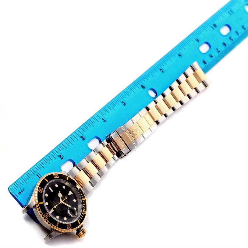 The image shows a Rolex Submariner 16613 Men
s Steel and Gold (two tone) Black Dial 16613 Men
s Steel and Gold (two tone) Black Dial watch with a blue ruler placed beside the watch to measure the bracelet length.
