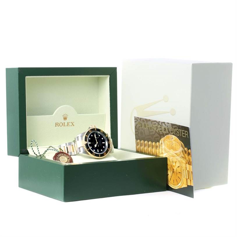 The image shows a Rolex Submariner 16613 Men
s Steel and Gold (two tone) Black Dial 16613 Men
s Steel and Gold (two tone) Black Dial watch at an angle within its open green box, along with a warranty card and tag.
