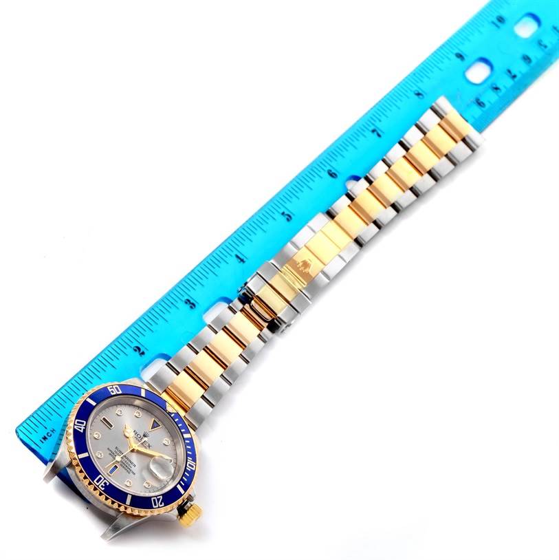 This image shows a close-up of a Rolex Submariner 16613 Men's Steel and Gold (two tone) Grey Dial 16613 Men's Steel and Gold (two tone) Grey Dial watch, with its full bracelet next to a blue measurement ruler.