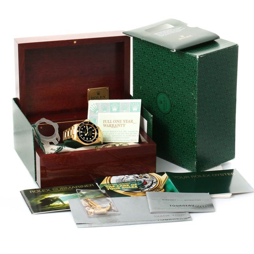 The image shows a Rolex Submariner 16618 Men
s Yellow Gold Black Dial 16618 Men
s Yellow Gold Black Dial watch along with its packaging, warranty card, manuals, and accessories, all displayed inside and around an open wooden box.