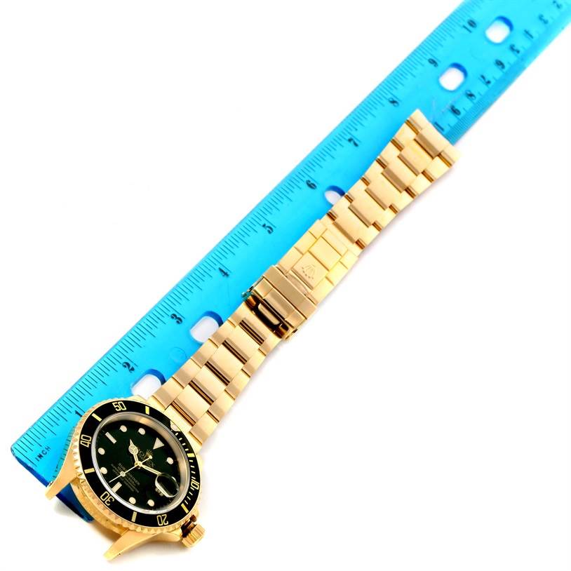 The Rolex Submariner 16618 Men
s Yellow Gold Black Dial 16618 Men
s Yellow Gold Black Dial watch is shown flat, with the face, bezel, crown, and bracelet in full view, next to a blue ruler for scale.