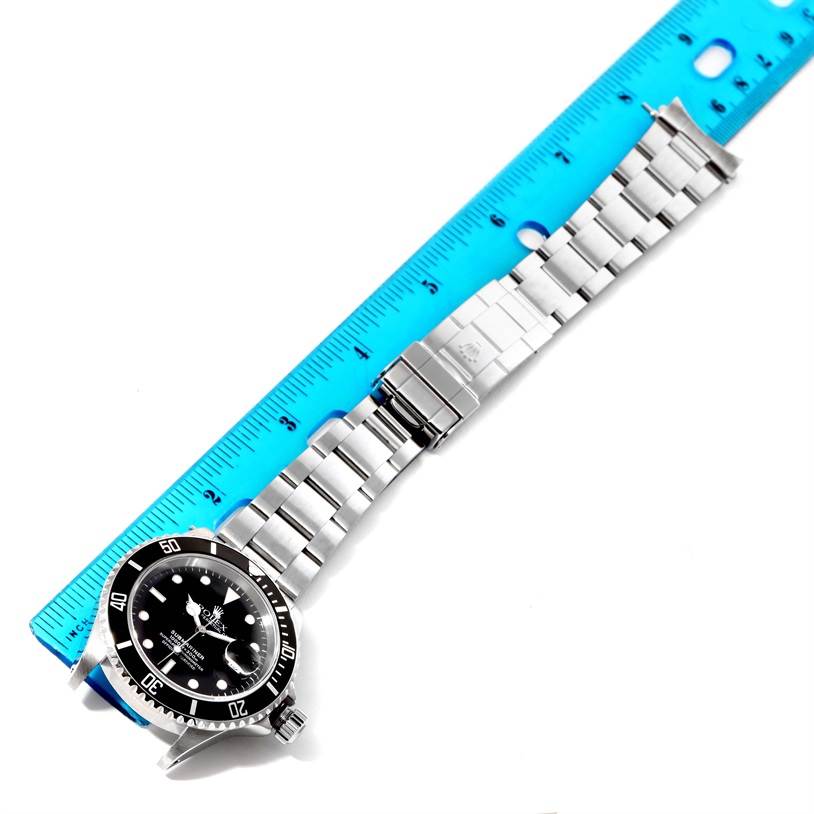 This image shows a Rolex Submariner 16610 Men
s Stainless Steel Black Dial 16610 Men
s Stainless Steel Black Dial watch laid flat on a surface with a blue ruler for scale, displaying the full bracelet and face.