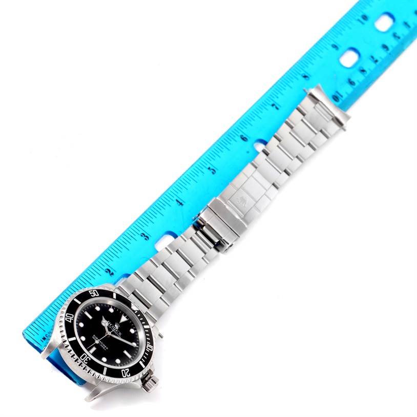 The Rolex Submariner 14060 Men
s Stainless Steel Black Dial 14060 Men
s Stainless Steel Black Dial watch is positioned diagonally, displaying its face and entire metal bracelet against a blue ruler for scale.