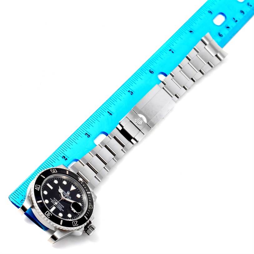 This image shows a Rolex Submariner 116610 Men
s Stainless Steel Black Dial 116610 Men
s Stainless Steel Black Dial watch laid flat with a blue measuring ruler along its length.