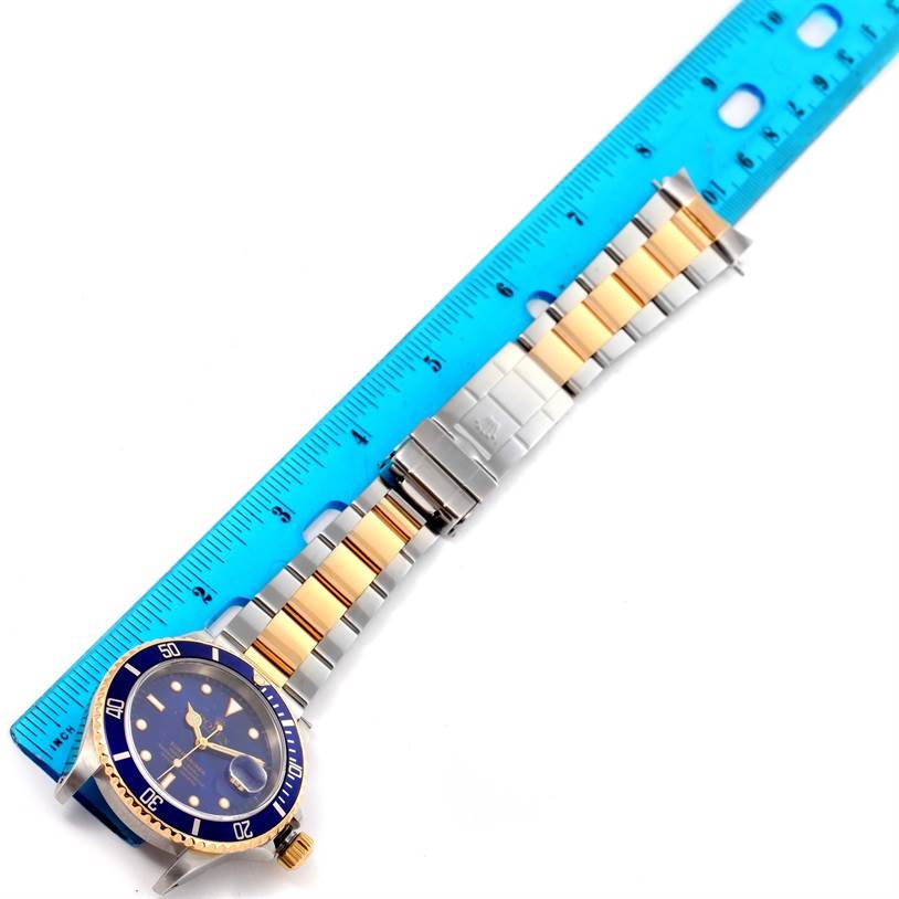 The Rolex Submariner 16613 Men
s Steel and Gold (two tone) Black Dial 16613 Men
s Steel and Gold (two tone) Black Dial watch is shown flat, displaying the face, bezel, crown, and metal bracelet alongside a blue ruler for scale.