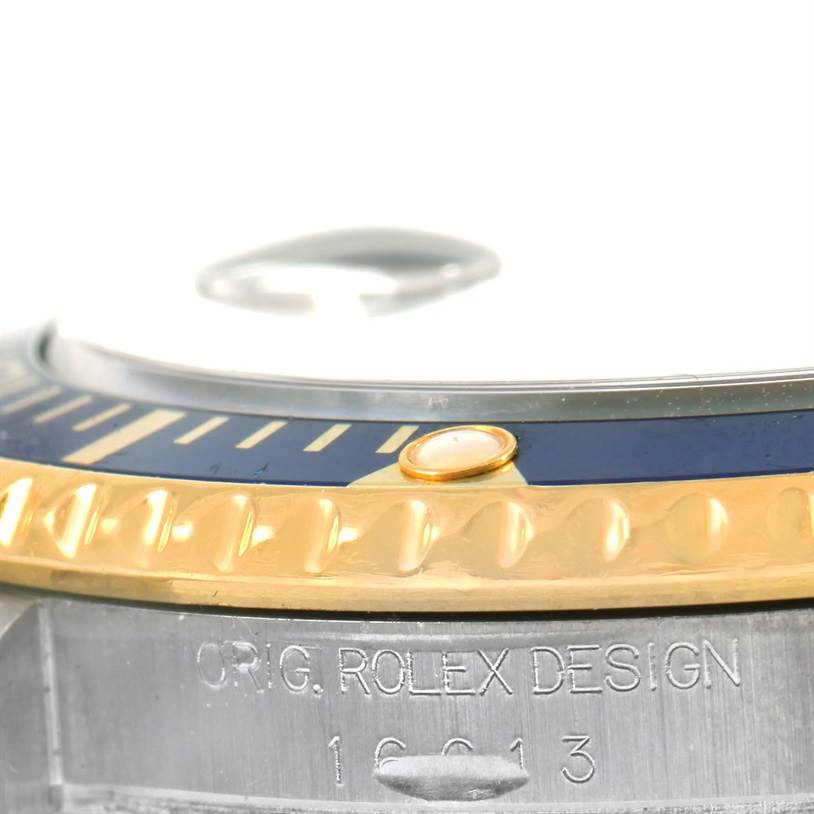 This close-up angle of the Rolex Submariner 16613 Men
s Steel and Gold (two tone) Black Dial 16613 Men
s Steel and Gold (two tone) Black Dial watch shows the bezel, case, and part of the crystal with the engraved model number.