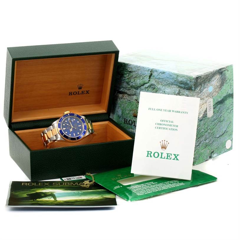 The Rolex Submariner 16613 Men
s Steel and Gold (two tone) Black Dial 16613 Men
s Steel and Gold (two tone) Black Dial watch is displayed inside an open green box, with documents and the outer box visible.