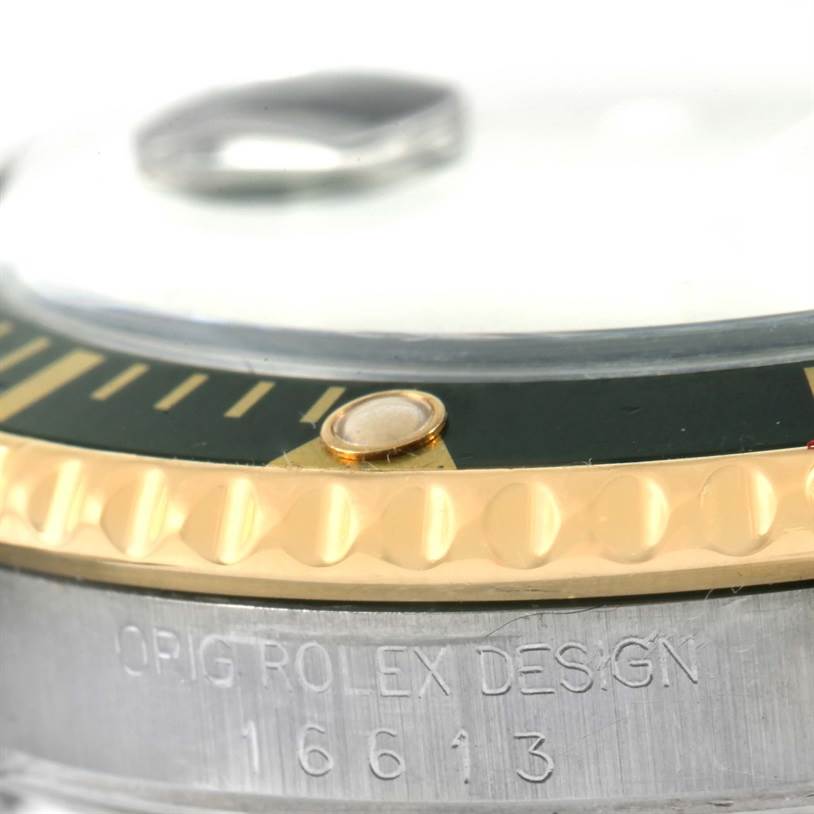 The image shows a close-up angle of the Rolex Submariner 16613 Men
s Steel and Gold (two tone) Black Dial 16613 Men
s Steel and Gold (two tone) Black Dial
s bezel and case, highlighting the engraved model number 16613.