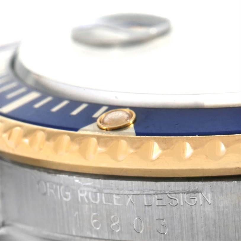 This is a close-up of a Rolex Submariner 16803 Men's Steel and Gold (two tone) Blue Dial 16803 Men's Steel and Gold (two tone) Blue Dial showing the bezel, crystal, and part of the engraved case.