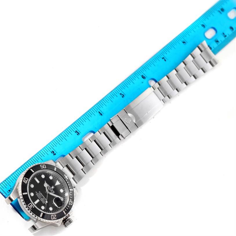 The image shows a top view of a Rolex Submariner 116610 Men
s Stainless Steel Black Dial 116610 Men
s Stainless Steel Black Dial watch with its bracelet laid straight alongside a blue ruler.