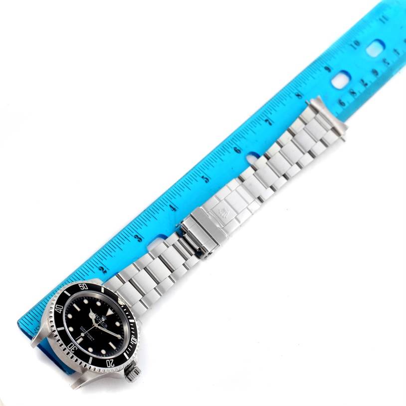 The image shows a Rolex Submariner 14060 Men
s Stainless Steel Black Dial 14060 Men
s Stainless Steel Black Dial watch laid flat with its bracelet fully extended alongside a blue measuring ruler.