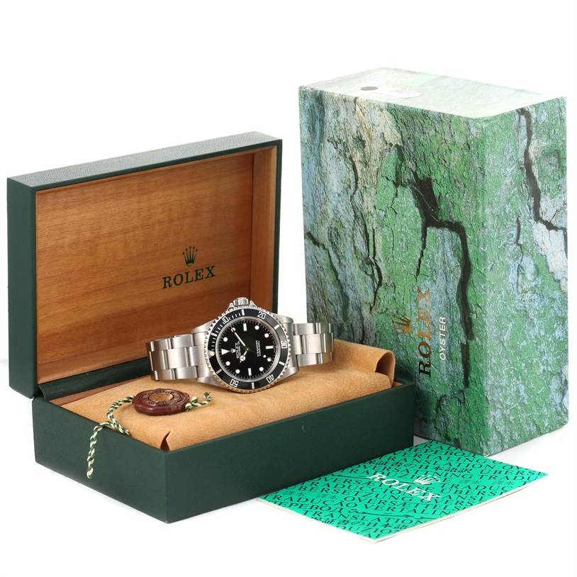 The image shows a Rolex Submariner 14060 Men
s Stainless Steel Black Dial 14060 Men
s Stainless Steel Black Dial watch displayed at an angle inside its open box, with booklet and accessories beside it.