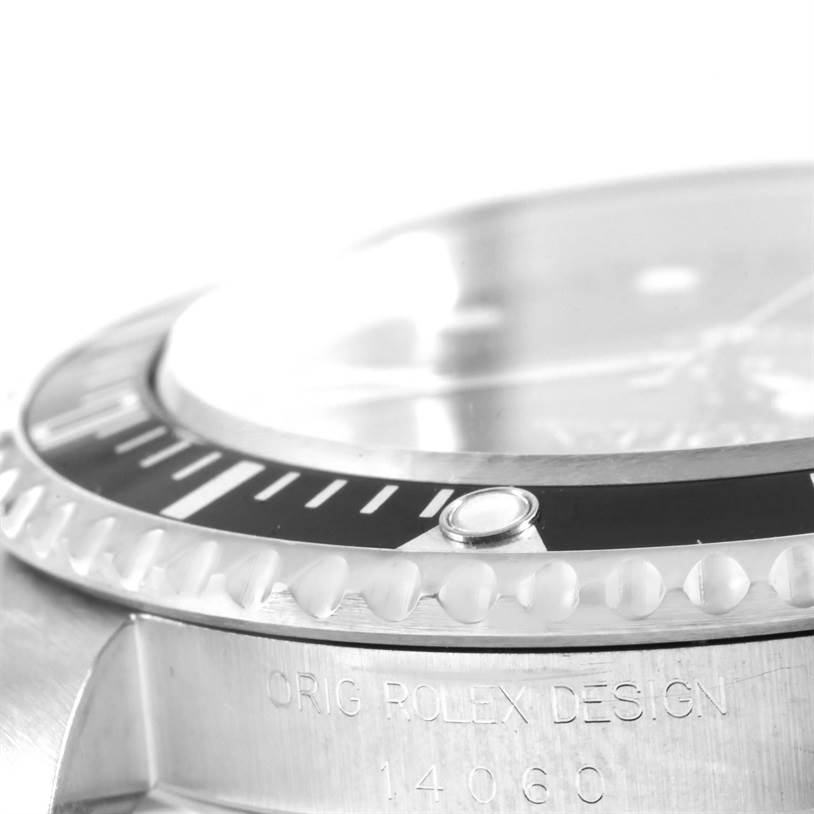 This close-up image of a Rolex Submariner 14060 Men
s Stainless Steel Black Dial 14060 Men
s Stainless Steel Black Dial shows the bezel, crystal, and part of the case with engraved text.