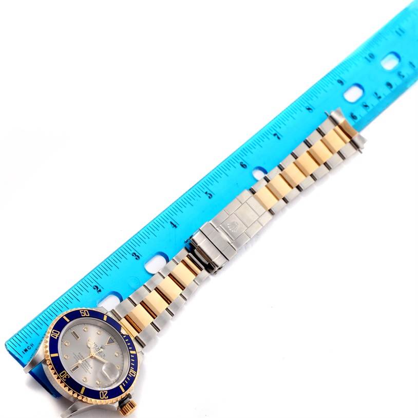 The image shows a Rolex Submariner 16613 Men
s Steel and Gold (two tone) Grey Dial 16613 Men
s Steel and Gold (two tone) Grey Dial watch laid flat next to a blue ruler, displaying the face, bezel, and bracelet.