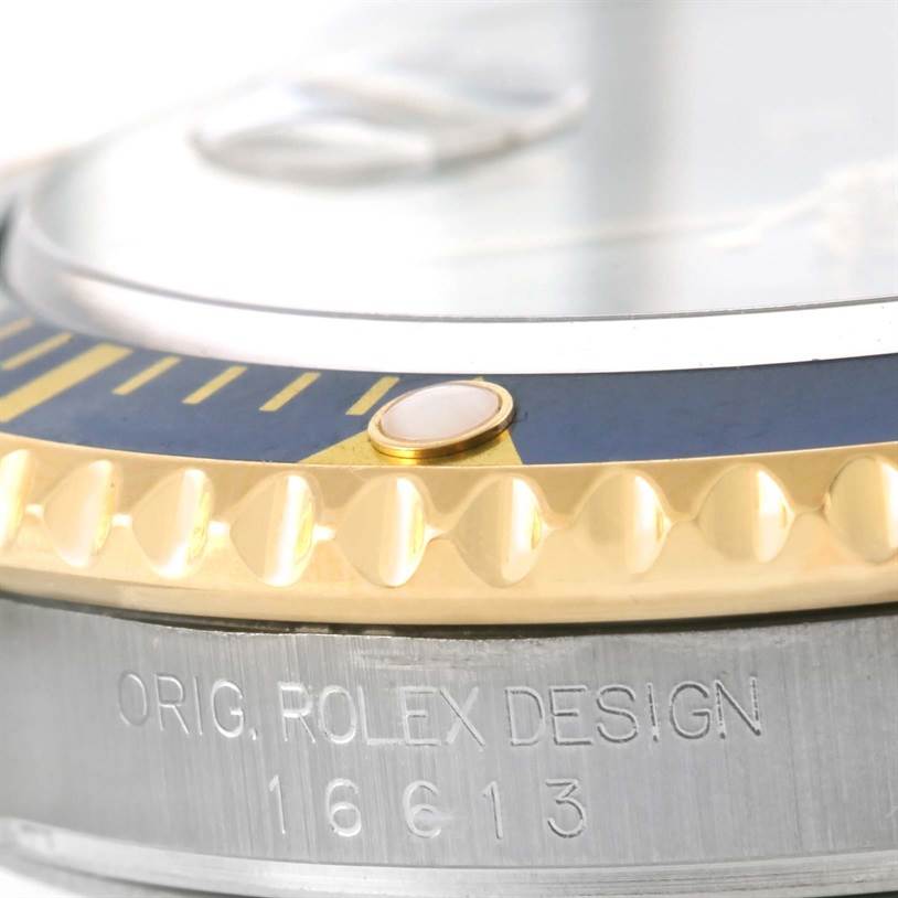 Close-up of the bezel and edge of the case of a Rolex Submariner 16613 Men
s Steel and Gold (two tone) Grey Dial 16613 Men
s Steel and Gold (two tone) Grey Dial watch, showing the engraving "ORIG. ROLEX DESIGN" and model number.