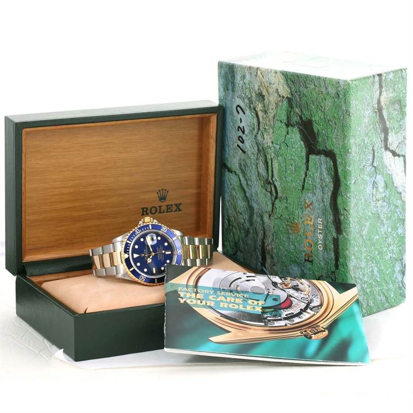 The image shows a Rolex Submariner 16613 Men
s Steel and Gold (two tone) Black Dial 16613 Men
s Steel and Gold (two tone) Black Dial watch, its box, and user manual from a frontal angle.