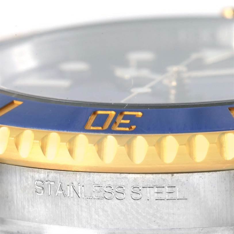 The image shows a close-up angle of the Rolex Submariner 116613 Men's Steel and Gold (two tone) Blue Dial 116613 Men's Steel and Gold (two tone) Blue Dial watch's bezel and case, highlighting the blue and gold bezel and the "STAINLESS STEEL" engraving.