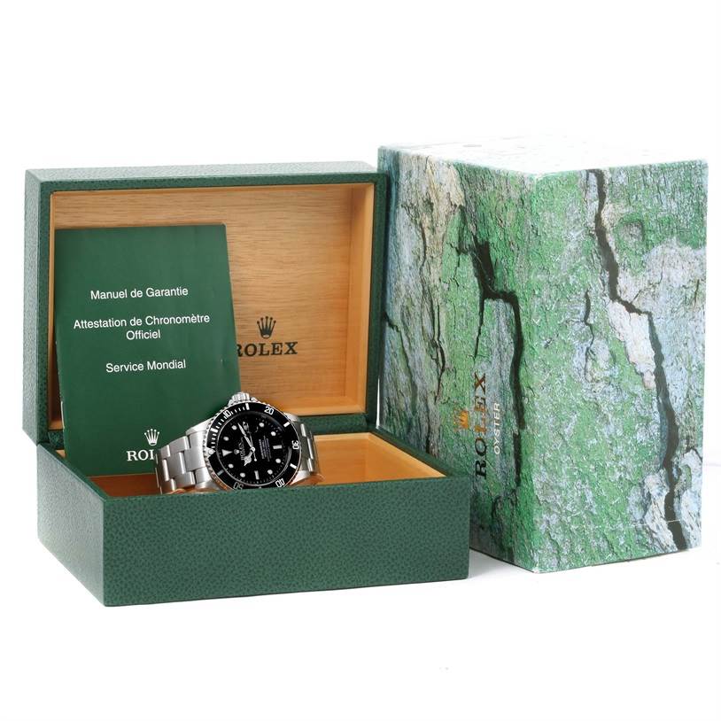 The image shows a Rolex Submariner 16610 Men
s Stainless Steel Black Dial 16610 Men
s Stainless Steel Black Dial watch in an open green box with accompanying documents and an outer sleeve.