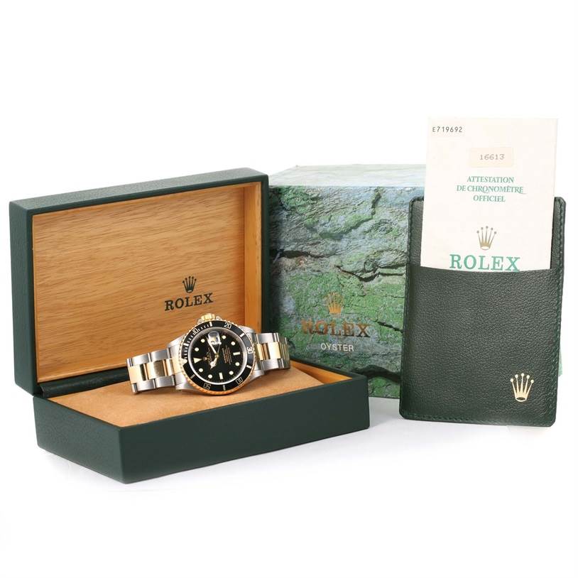 The Rolex Submariner 16613 Men's Steel and Gold (two tone) Black Dial 16613 Men's Steel and Gold (two tone) Black Dial watch is displayed in its open box with accompanying documentation and a green cardholder.